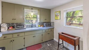 A kitchen with light green cabinets, a microwave, a toaster, and a window with a view of trees.