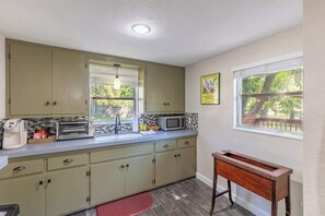 Une cuisine avec des meubles de couleur vert clair, un four à micro-ondes, un grille-pain et une fenêtre donnant sur des arbres.