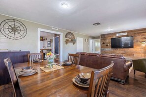 Un comedor con mesa de madera, sillas y un televisor instalado en una pared de madera.