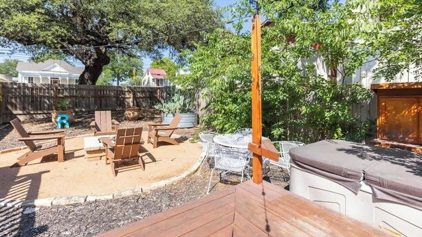Un jardin avec une terrasse en bois, un coin salon extérieur et un grand arbre.