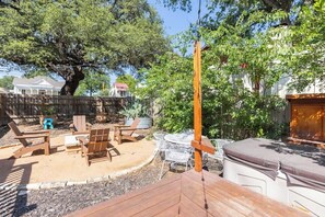 A backyard with a wooden deck, outdoor seating, and a large tree. - Downtown Bliss: Hot Tub (Fredericksburg)