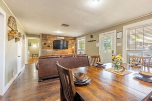 A dining area with a wooden table, chairs, and a television mounted on a wooden wall. - Downtown Bliss: Hot Tub (Fredericksburg)