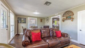 Un salon spacieux avec un canapé en cuir marron, une table basse et un coin repas à l’arrière-plan.