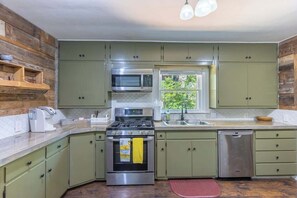 A kitchen with green cabinets, a stainless steel stove, a microwave, and a dishwasher.
