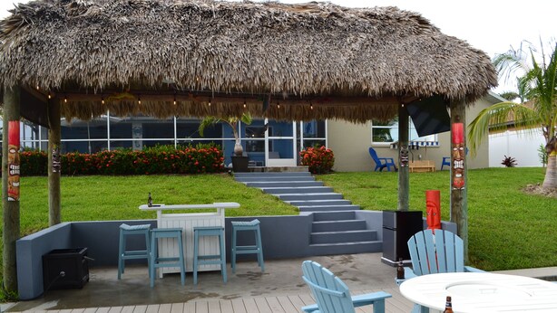 A covered outdoor area with a thatched roof, a pool, and a seating area with chairs and tables.