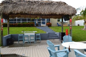 A covered outdoor area with a thatched roof, a pool, and a seating area with chairs and tables. - Family Friendly, Heated pool, dock tiki bar Bikes basketball scooters Basketball (Cape Coral)