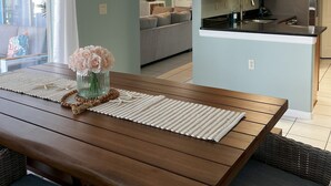 A modern kitchen with wooden cabinets, a stainless steel refrigerator, and a dining area with a wooden table and wicker chairs.