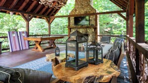 An outdoor wooden deck with a stone fireplace, a round wooden table, and two lanterns. - Bentley's Retreat On Overlook (Blue Ridge)