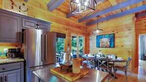 A wooden cabin interior with a kitchen, dining area, and a large window. - Bentley's Retreat On Overlook (Blue Ridge)