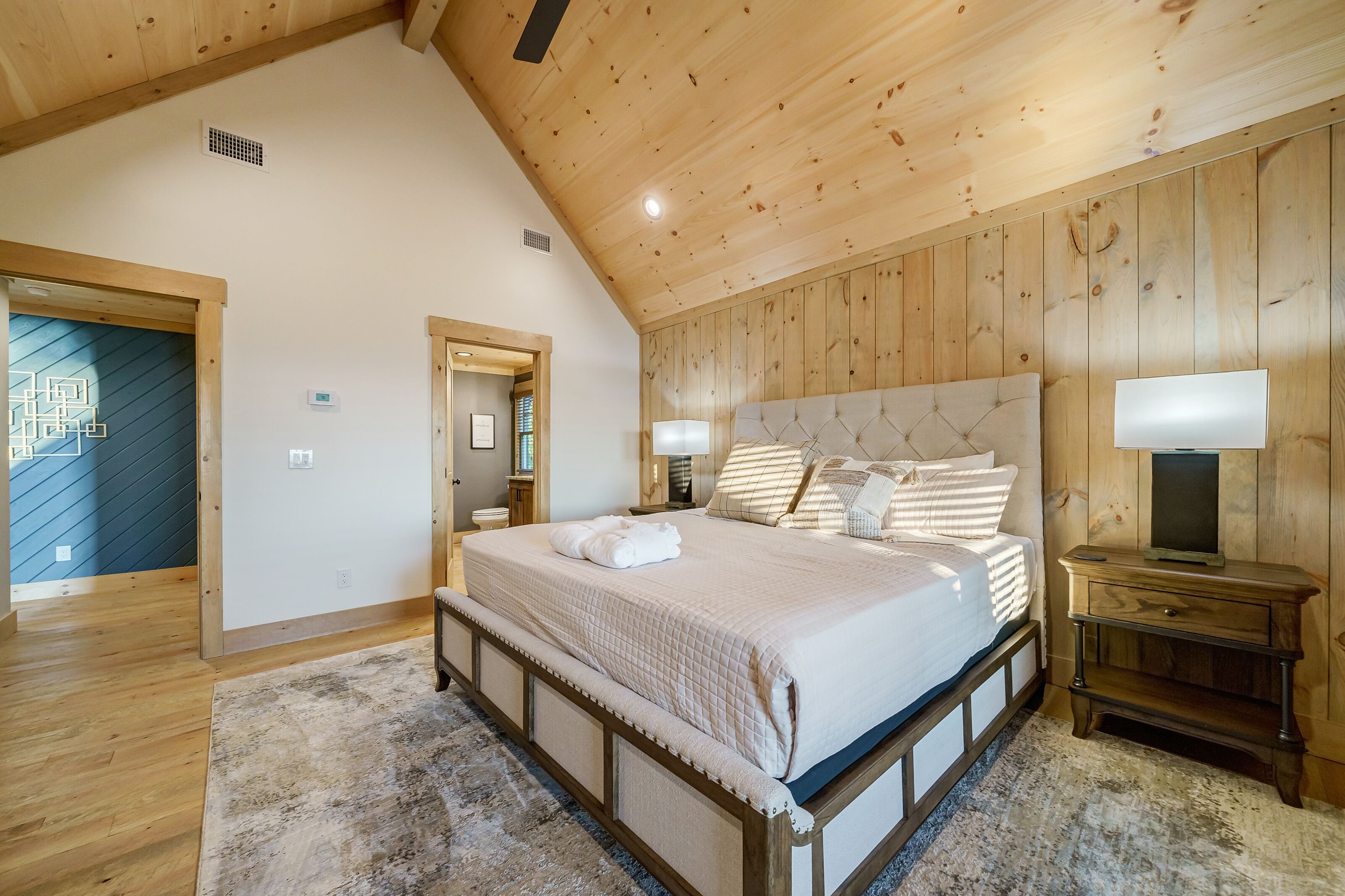 A bedroom with a wooden ceiling, a bed with a headboard, a nightstand, and a bedside table.