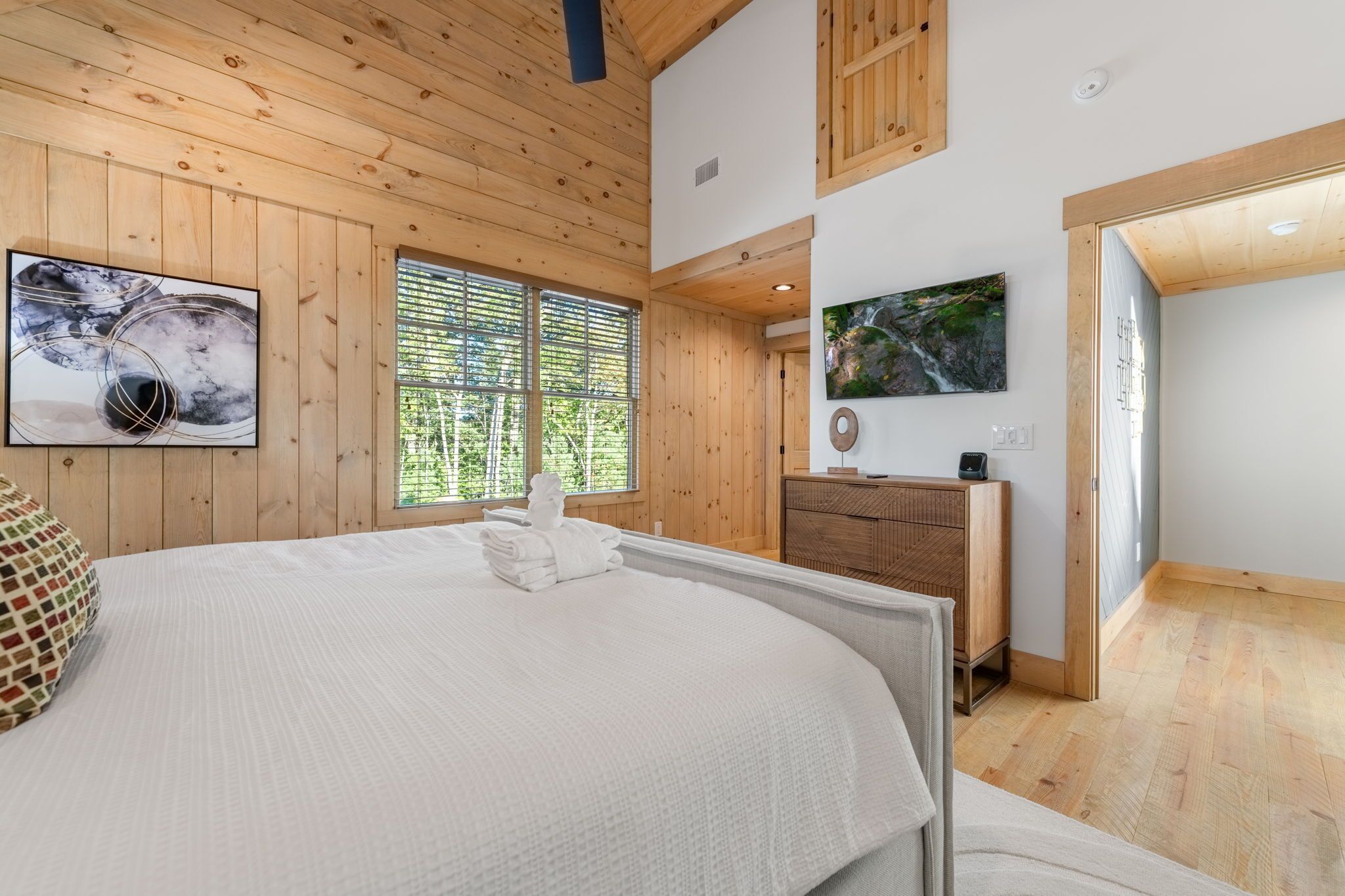 Un dormitorio con una cama grande, techo de madera y una ventana con persianas.