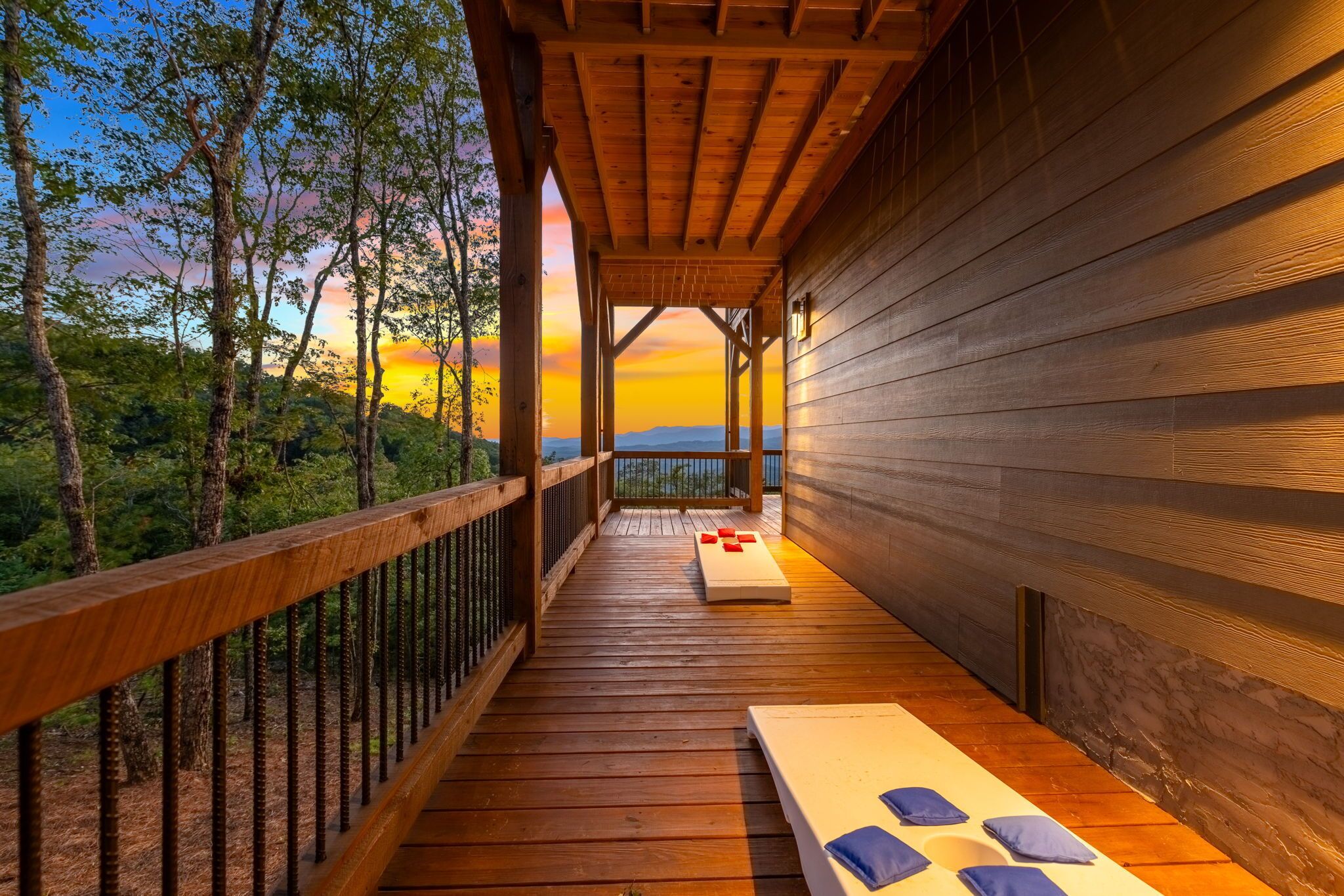A wooden deck with a view of the sunset, a white bench, and a table with cushions.