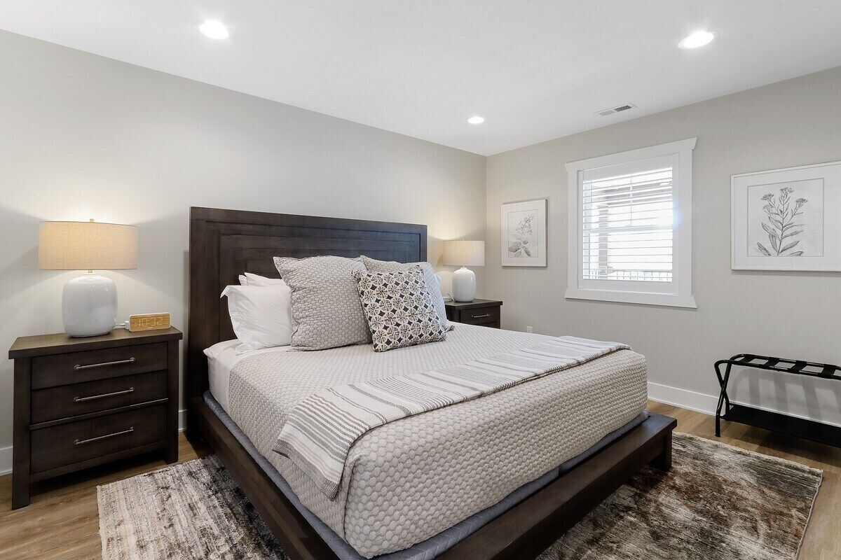 Une chambre à coucher avec un grand lit, deux tables de chevet, une commode et une fenêtre avec des stores.