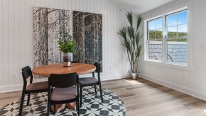 A dining area with a round wooden table, black chairs, and a patterned floor. There is a large window with a view of a building and a tree outside. - The Lofts of Brick and Mortar-City Loft |Stylish |Walk-Out Balcony |2 Kings |Parking for 2 |Downtown (Lake Geneva)