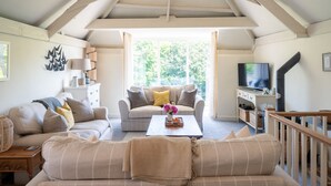 Een gezellige woonkamer met een hoge plafond, een zithoek, een bijzettafeltje met bloemen, een televisie en een open haard.