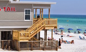A beachside building with a wooden staircase leading to a deck, a lifeguard tower, and beachgoers in the background. - Near Beach🏖️Multiple Pools-Golf-Onsite Restaurants-3BR Beach Baby (Destin)
