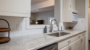 A modern kitchen with white cabinetry, a granite countertop, a stainless steel sink, and a built-in microwave.