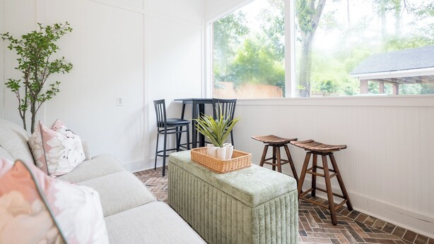 A bright room with a large window, a sofa, a small table, and a chair.
