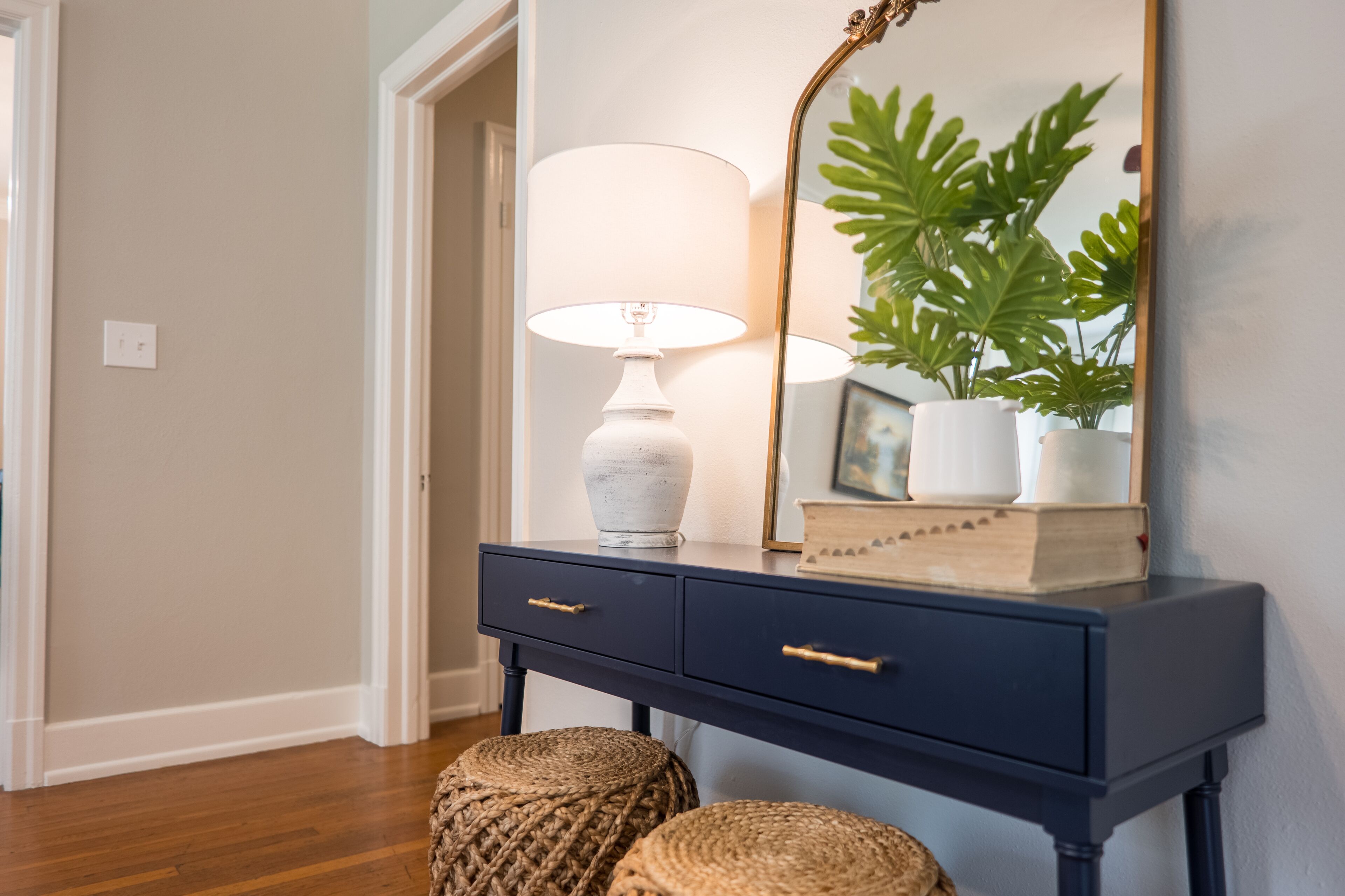 A dark blue console table with a white lamp, a mirror, and a potted plant.