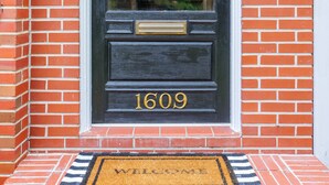 A black door with the number 1609, a doormat with "WELCOME" text, and a small wall-mounted light fixture.