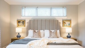 A bedroom with a large bed, two bedside tables with lamps, a headboard, and two framed pictures on the walls.