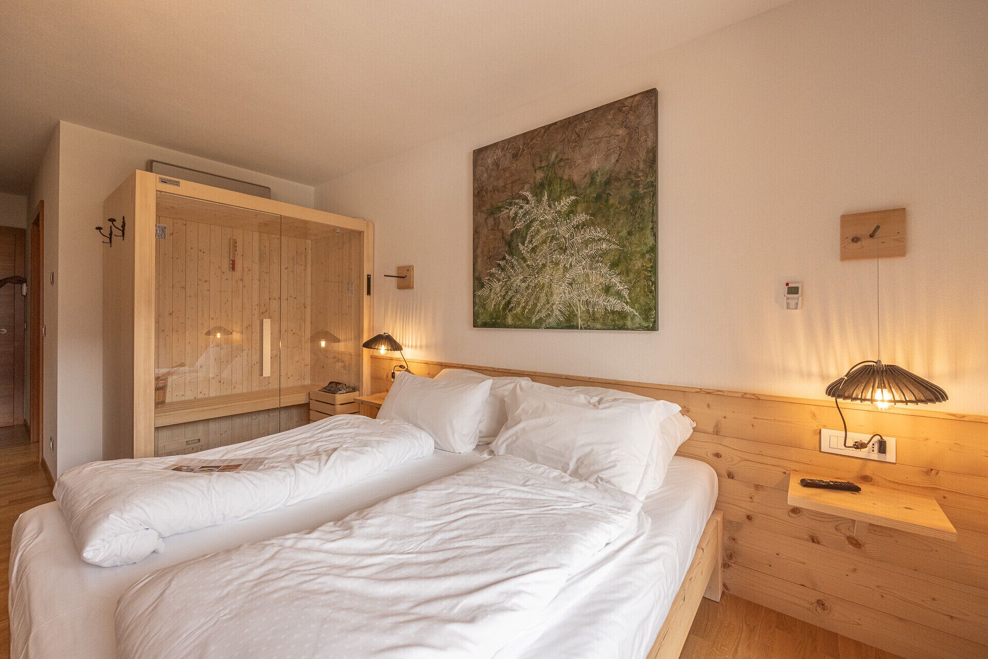 A room with two beds, wooden walls, a painting, and a nightstand with a lamp.