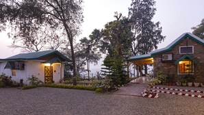 A rustic lodge with a gravel driveway, a covered porch, and a stone building with a green roof. - Seclude Nahan Bantony Cottage (Paonta Sahib)