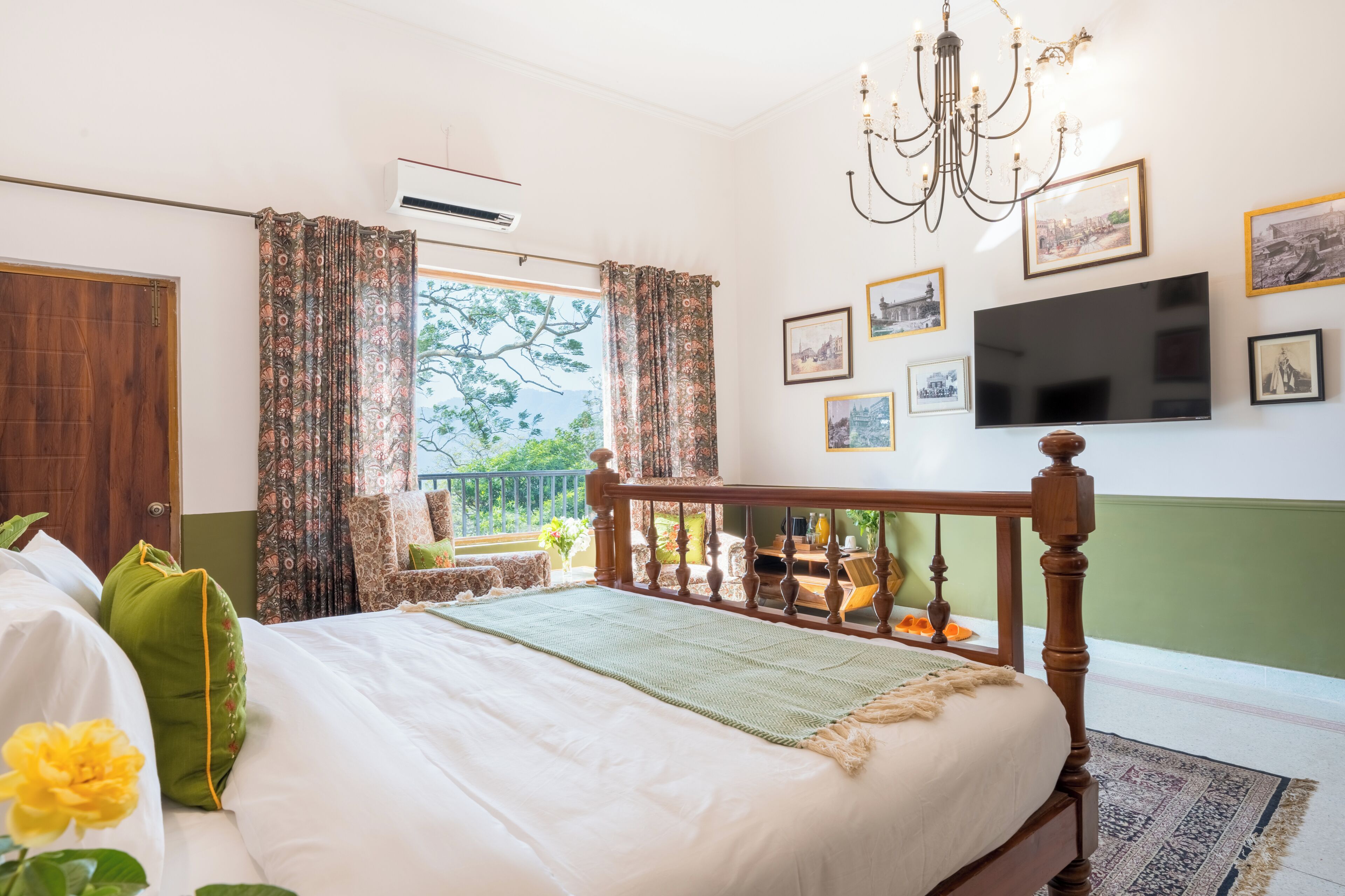 A bedroom with a bed, curtains, a chandelier, a TV, and framed pictures on the wall.