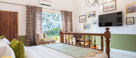 A bedroom with a bed, curtains, a chandelier, a TV, and framed pictures on the wall.