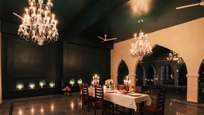 A formal dining room with a long table, chandeliers, and arched windows. - Seclude Nahan Bantony Cottage (Paonta Sahib)