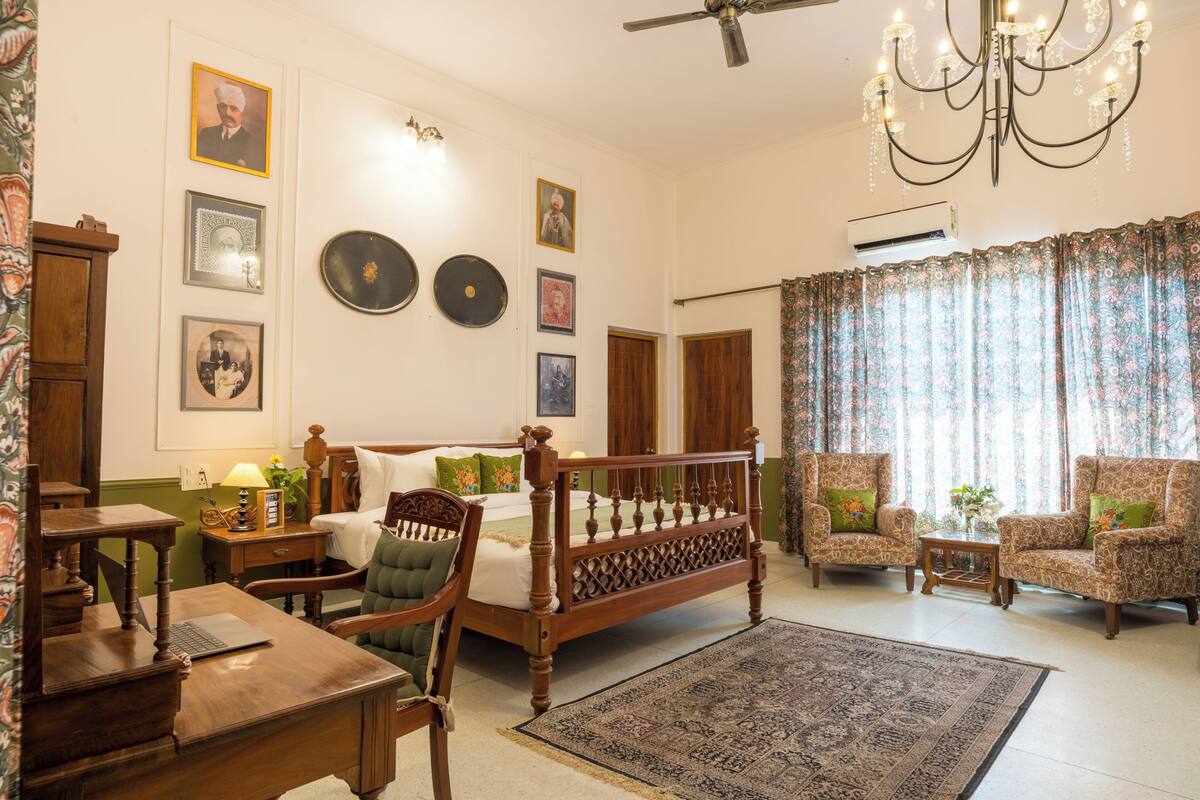 A traditional room with a bed, two armchairs, a desk, a chandelier, and wall-mounted decorations.