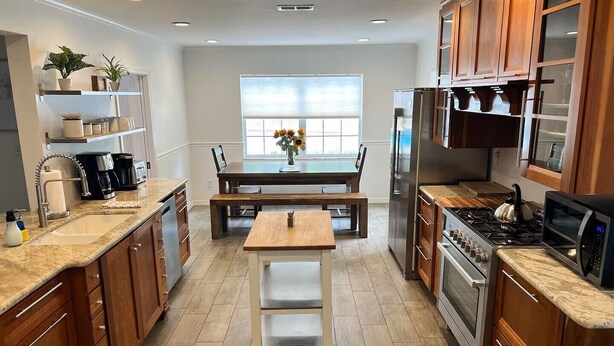Una cocina moderna con armarios de madera, un refrigerador de acero inoxidable, una estufa a gas y un comedor con mesa y sillas de madera.