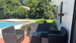 Un patio con mobiliario de mimbre, una piscina y un edificio blanco con una jardinera colgante.