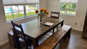 Un comedor con una mesa de madera, cuatro sillas, un banco y un florero con girasoles.