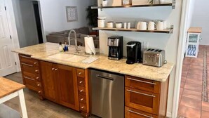 Una cocina con encimera de granito, lavavajillas de acero inoxidable, armarios de madera, cafetera y tostadora.