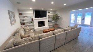 Una sala de estar con un sofá modular, un televisor de pantalla plana, una chimenea y una estantería.