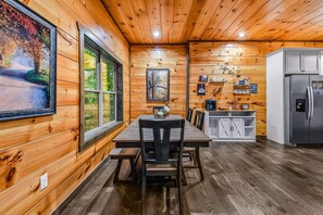 A wooden cabin interior with a dining table, chairs, a refrigerator, and a kitchen area.