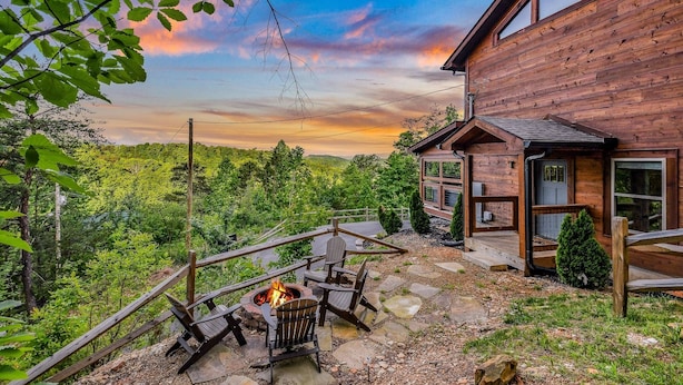Eine Holzhütte mit einer Steinterrasse, Sitzgelegenheiten im Freien und einer Feuerstelle.