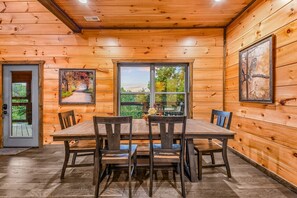 A wooden cabin interior with a dining table and chairs, a door, and two windows. - Bearly Behaving 2 Bedroom Cabin by RedAwning (Sevierville)