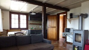 Uma sala de estar aconchegante com um sofá, uma área de jantar com mesa e cadeiras, uma cozinha com armários de madeira, micro-ondas e um fogão a lenha.