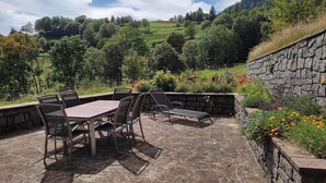 Um pátio externo com chão de pedra, uma mesa com cadeiras e uma parede de pedra.
