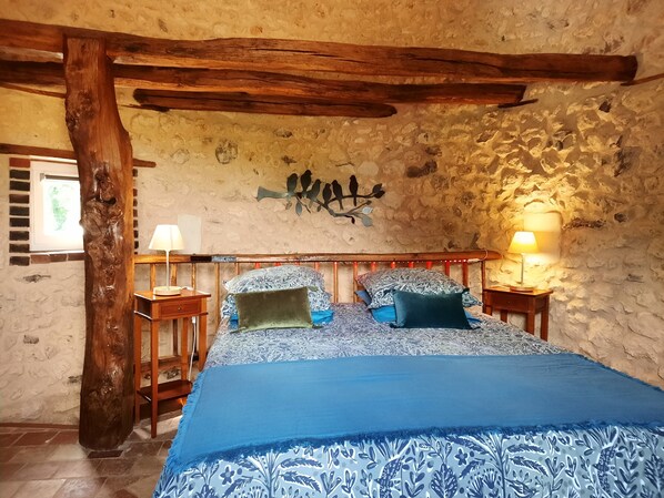 Une chambre à coucher rustique avec des murs en pierre apparentes, un cadre de lit en bois et un grand tronc d’arbre.