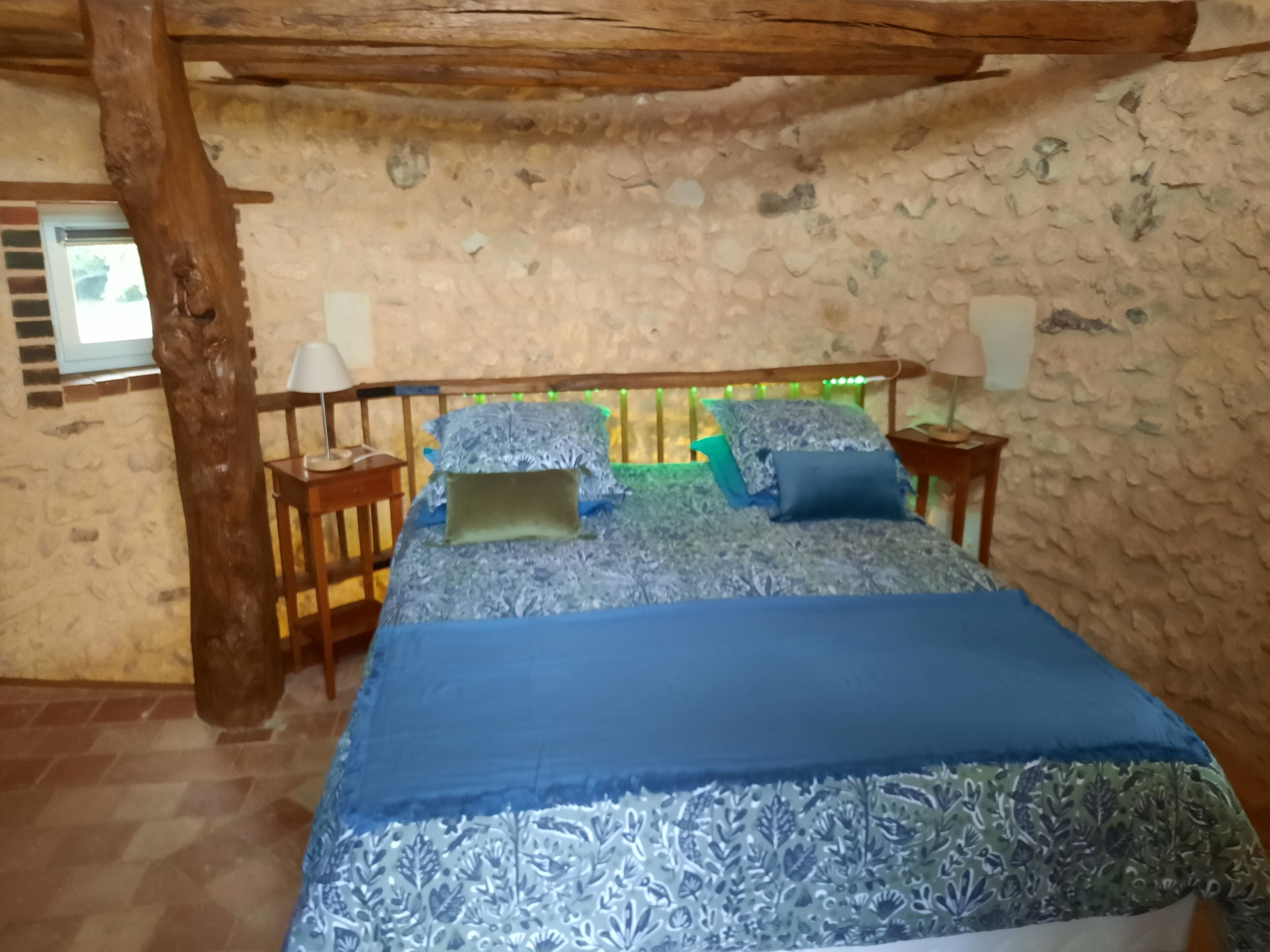 Una camera da letto con parete in pietra, struttura del letto in legno, copripiumino blu e due lampade da comodino.