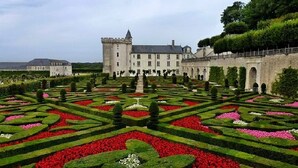 Un jardín formal con diseños geométricos y un edificio grande al fondo.