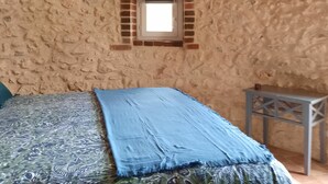 Una habitación rústica con una pared de piedra, una cama con colcha estampada, una mesita y una obra de arte enmarcada sobre la cama.