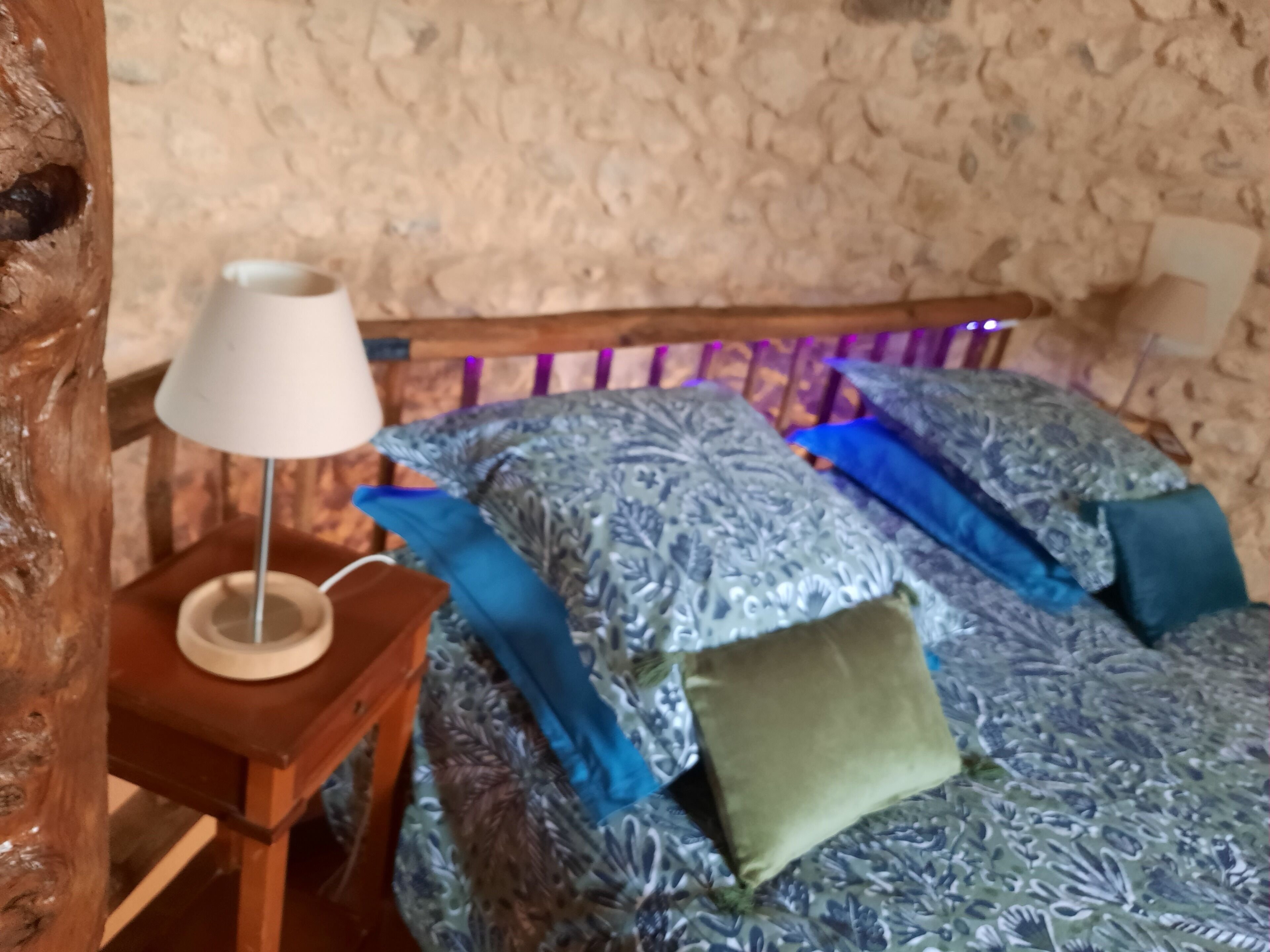 A bedroom with a patterned bedspread, a wooden headboard, and a bedside table with a lamp.