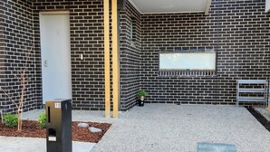Een gevel van zwart-wit baksteen, een metalen bankje, een kleine plantenbak met een plant en een metalen afvalbak.