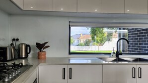 Een moderne keuken met een gasfornuis, een koffiezetapparaat, een waterkoker en een kamerplant.