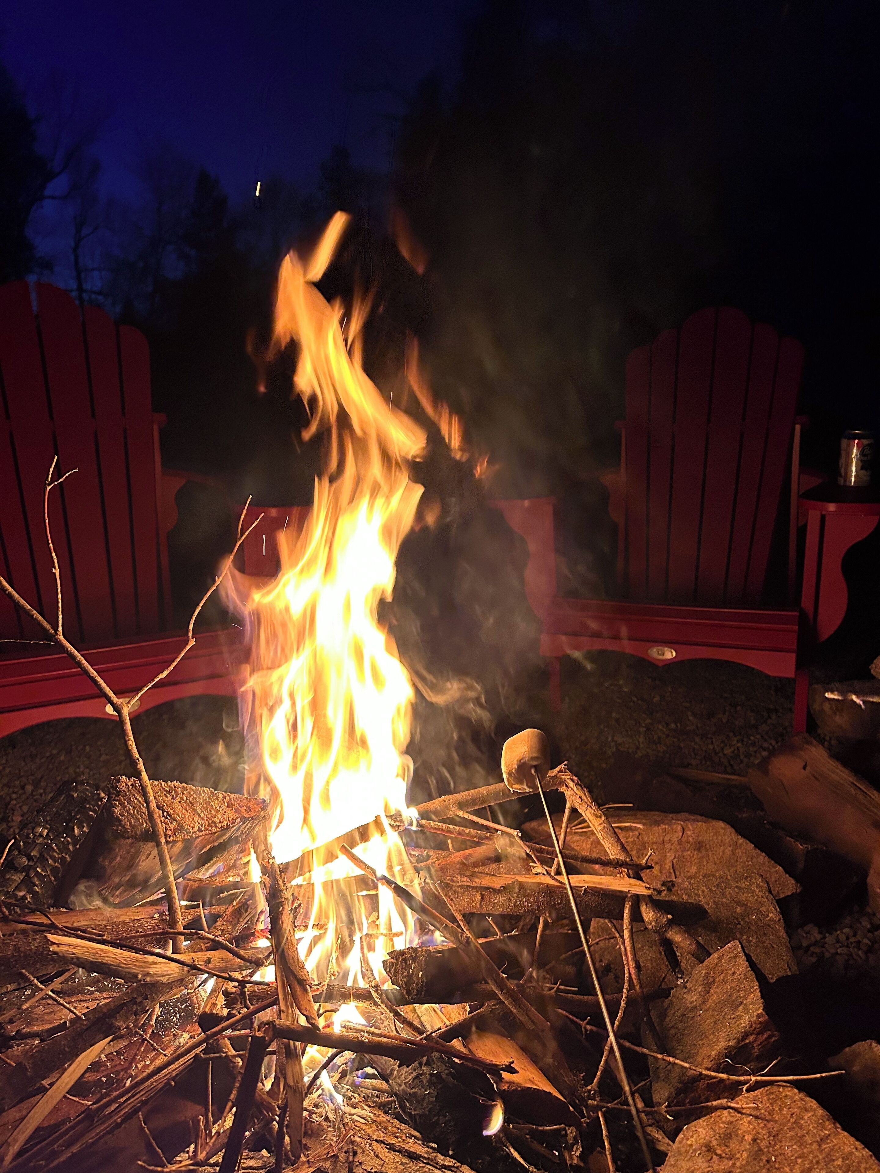 Ein Lagerfeuer mit roten Adirondack-Stühlen darum.