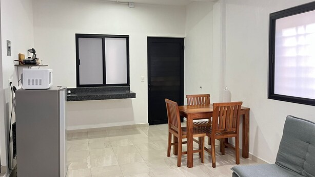 A compact living space with a kitchenette, a dining area with a table and chairs, a grey sofa, and a black door. - Studio on Cancun Downtown. Close to grocery stores, restaurants and bus stop. (Cancún)